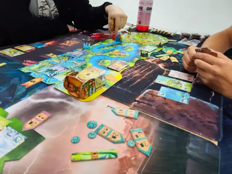 A game of Meadow at the club table — the board, landscape tiles, observation cards and a cardboard backpack holding a deck