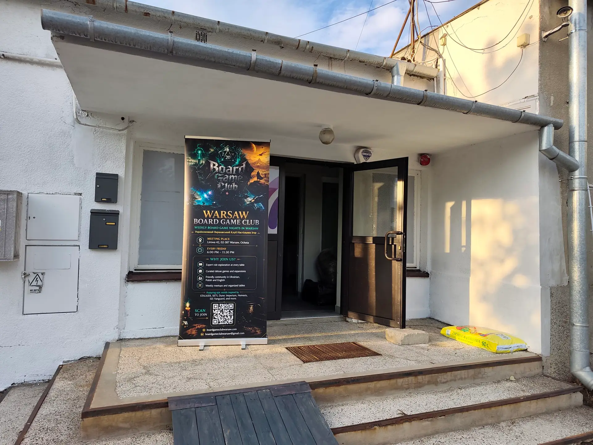 Entrance to Warsaw Board Game Club at Lirowa 42 in Ochota — a roll-up banner with meeting details beside the open door
